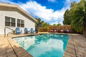 Uma piscina com deck de madeira, cercada por cadeiras e uma casa.