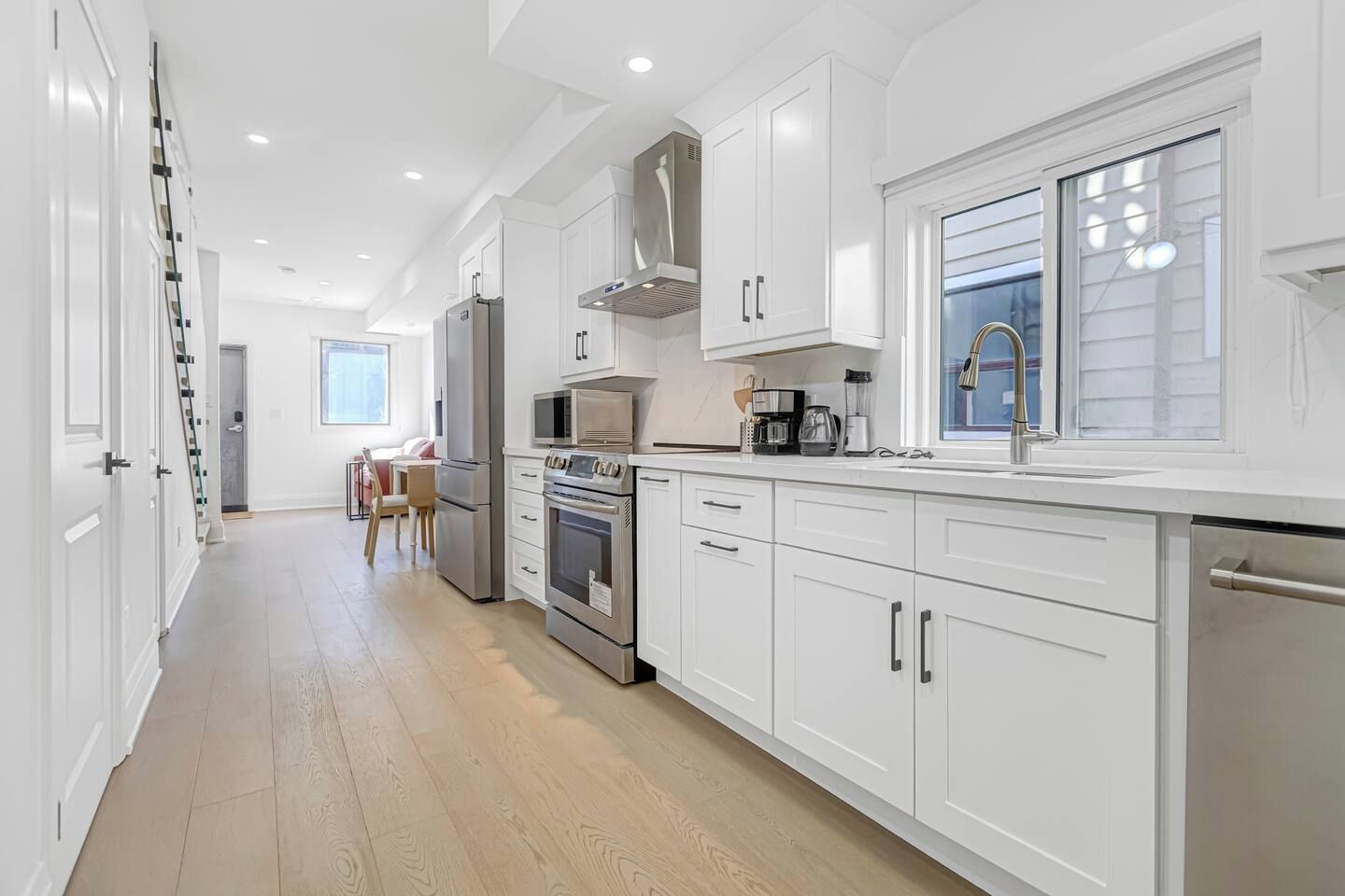 A modern kitchen with white cabinetry, stainless steel appliances, and a window providing natural light.