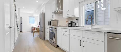 A modern kitchen with white cabinetry, stainless steel appliances, and a window providing natural light.