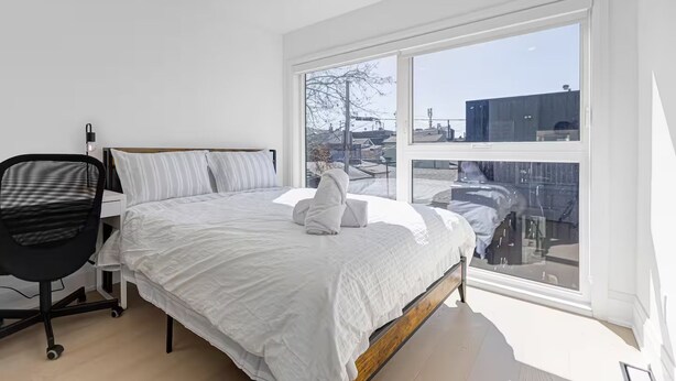 Een slaapkamer met een groot raam, een bed, een bureau en een stoel.