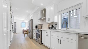 Een moderne keuken met witte kasten, roestvrijstalen apparatuur en een raam dat voor natuurlijk licht zorgt.