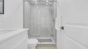 Een moderne badkamer met een douchecabine van glas, een wit toilet en een wastafel met spiegel.
