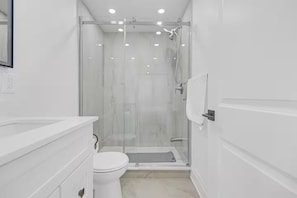 Ein modernes Badezimmer mit einer Duschkabine aus Glas, einer weißen Toilette und einem Waschtisch mit Spiegel.