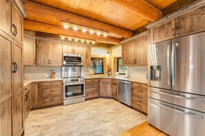 A modern kitchen with wooden cabinets, stainless steel appliances, and a marble floor. - Riverfront Cabin on the Swan | Fire Pit & Fishing (Bigfork)
