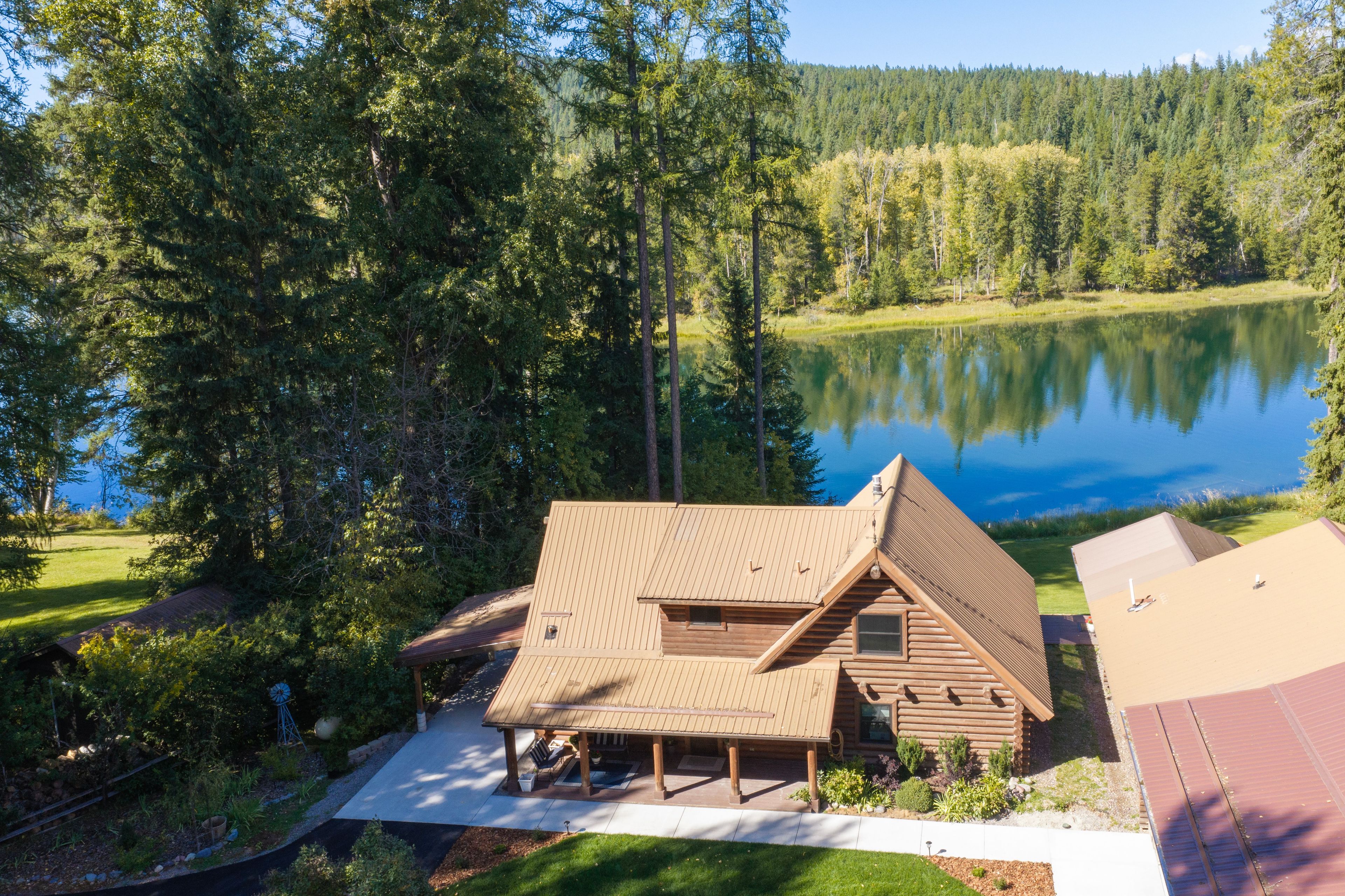 A cabin with a sloped roof, a porch, and a view of a lake surrounded by trees.