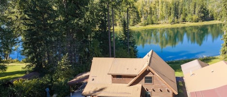 A cabin with a sloped roof, a porch, and a view of a lake surrounded by trees.