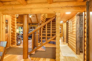 A wooden interior with a staircase, bookshelves, and a cozy seating area. - Riverfront Cabin on the Swan | Fire Pit & Fishing (Bigfork)