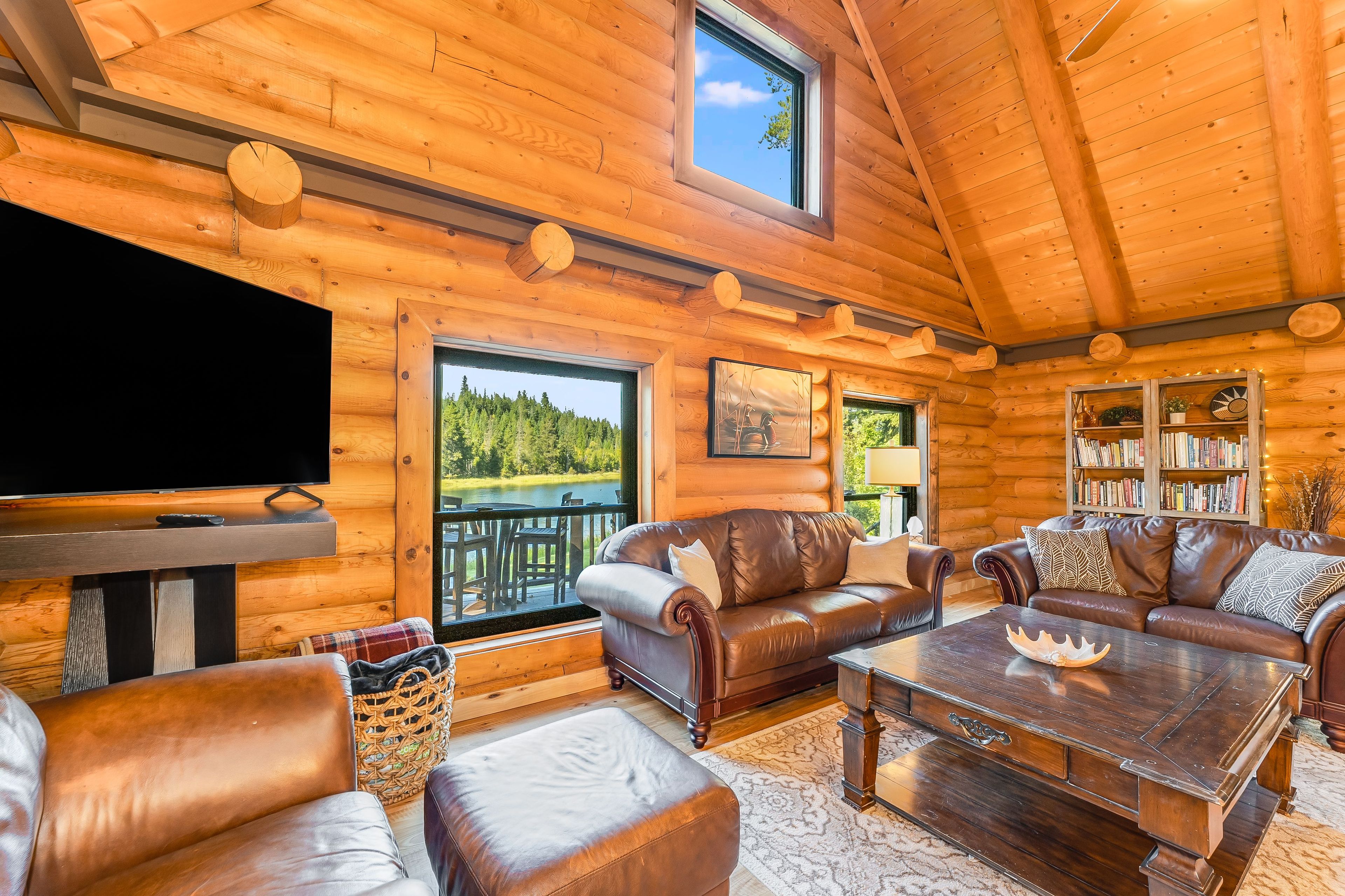 A log cabin interior with a TV, leather sofas, a coffee table, and a bookshelf.