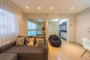 Una sala moderna con un sofá, cojines estampados, un sillón de peluche oscuro y una silla blanca.