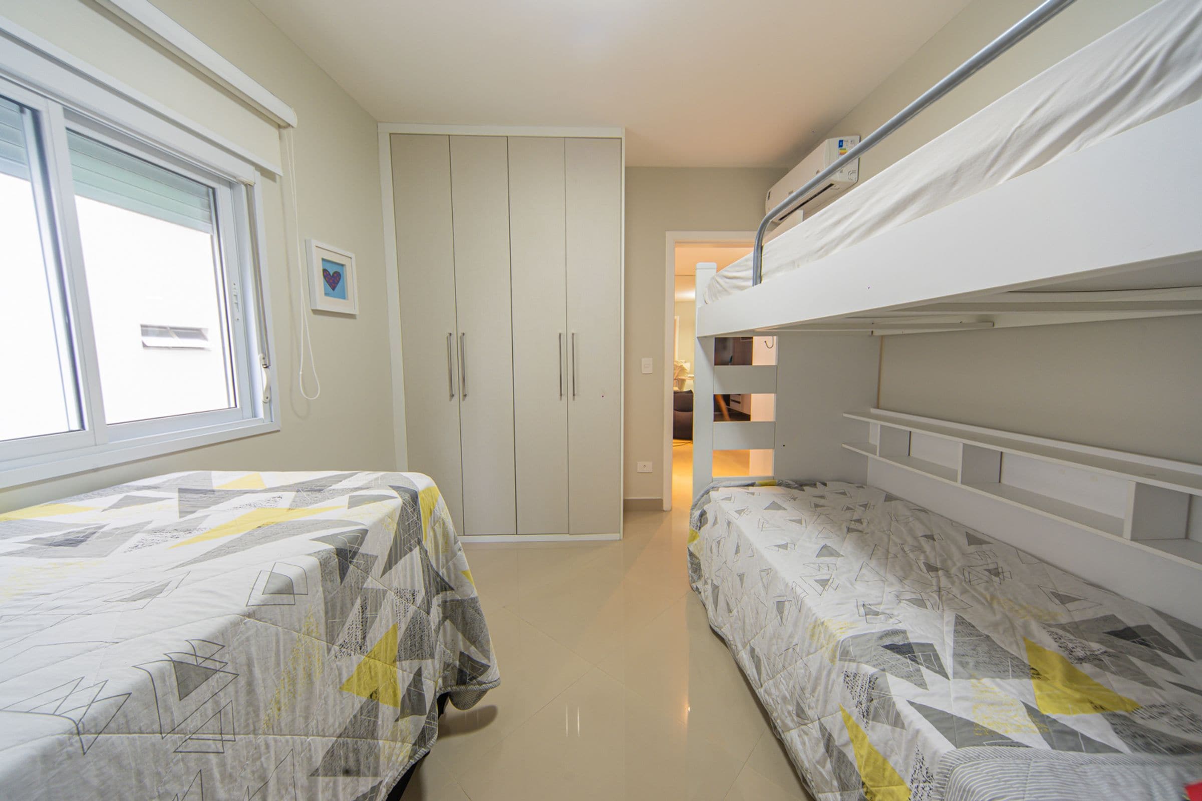 A narrow room with two beds, a wardrobe, and a window.