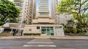 Un edificio residencial de varios pisos con entrada protegida por un portón, un número de dirección visible y un paso de peatones en la fachada.