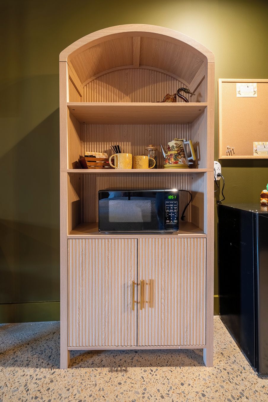 Una kitchenette con microondas, cafetera y hervidor sobre un mueble de madera.