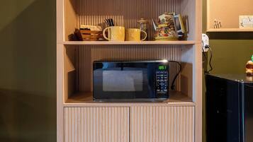 Una kitchenette con microondas, cafetera y hervidor sobre un mueble de madera.