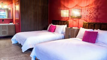 A hotel room with two beds, a vanity with a mirror, and a red accent wall.