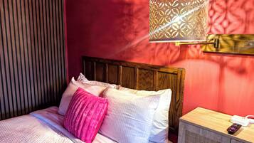Una cama con almohadas, una mesita de noche con un control remoto y una lámpara de pared.