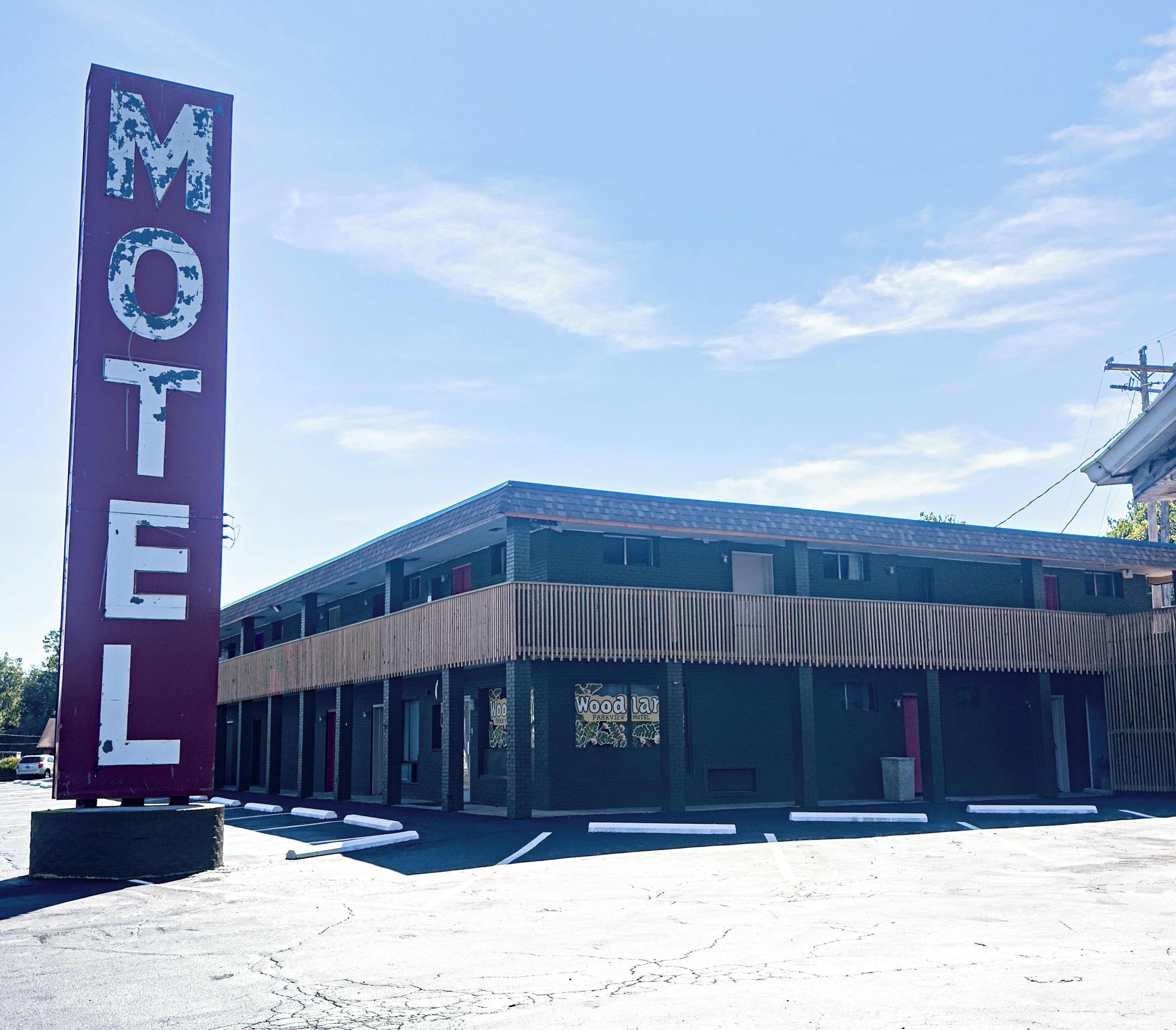 Un motel con un letrero grande, varias habitaciones y un estacionamiento.