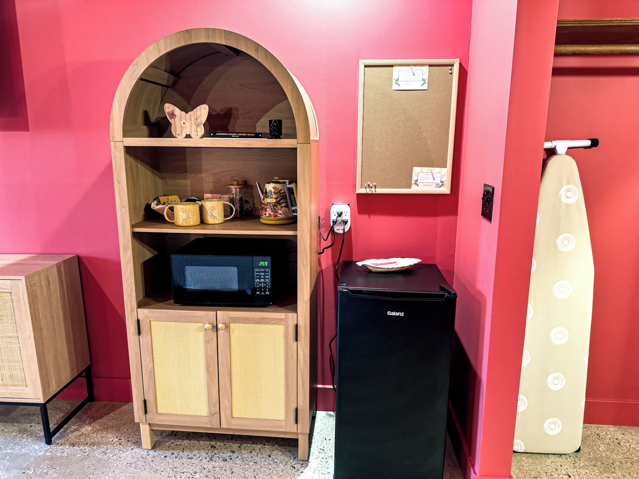 Una kitchenette equipada con microondas, un refrigerador pequeño y un estante con utensilios de cocina.