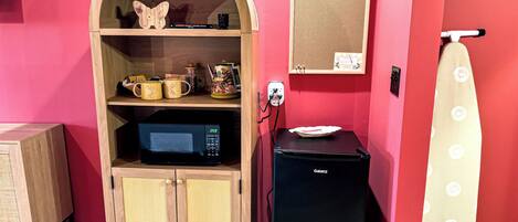 Uma cozinha compacta com micro-ondas, mini-geladeira e prateleira com utensílios de cozinha.
