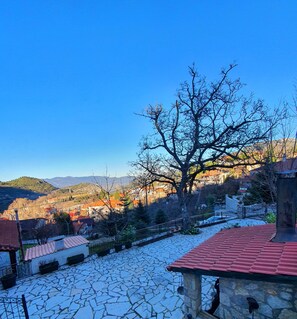 Ein Innenhof mit Steinpflaster, einem Baum und Blick auf eine Stadt mit Gebäuden und Hügeln im Hintergrund.
