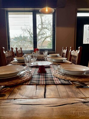 Mesa de comedor dispuesta para seis personas, con camino de mesa a cuadros, sillas de madera y un centro de mesa rojo.