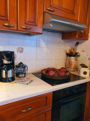 A kitchen with wooden cabinets, a stainless steel range hood, a coffee maker, a kettle, a bowl of red potatoes, and a wooden spice rack. - Eleni's Guesthouse Country House with Wi-Fi and Mountain Views (Επτάλοφος)
