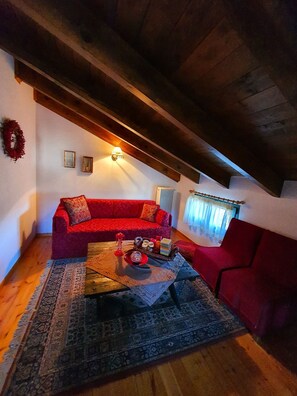 A cozy living room with a red sofa, a coffee table with decorative items, and a wooden ceiling. - Eleni's Guesthouse Country House with Wi-Fi and Mountain Views (Επτάλοφος)