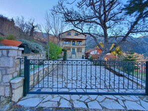 Uma casa de pedra com varanda, cercada por um portão de metal e muros de pedra.