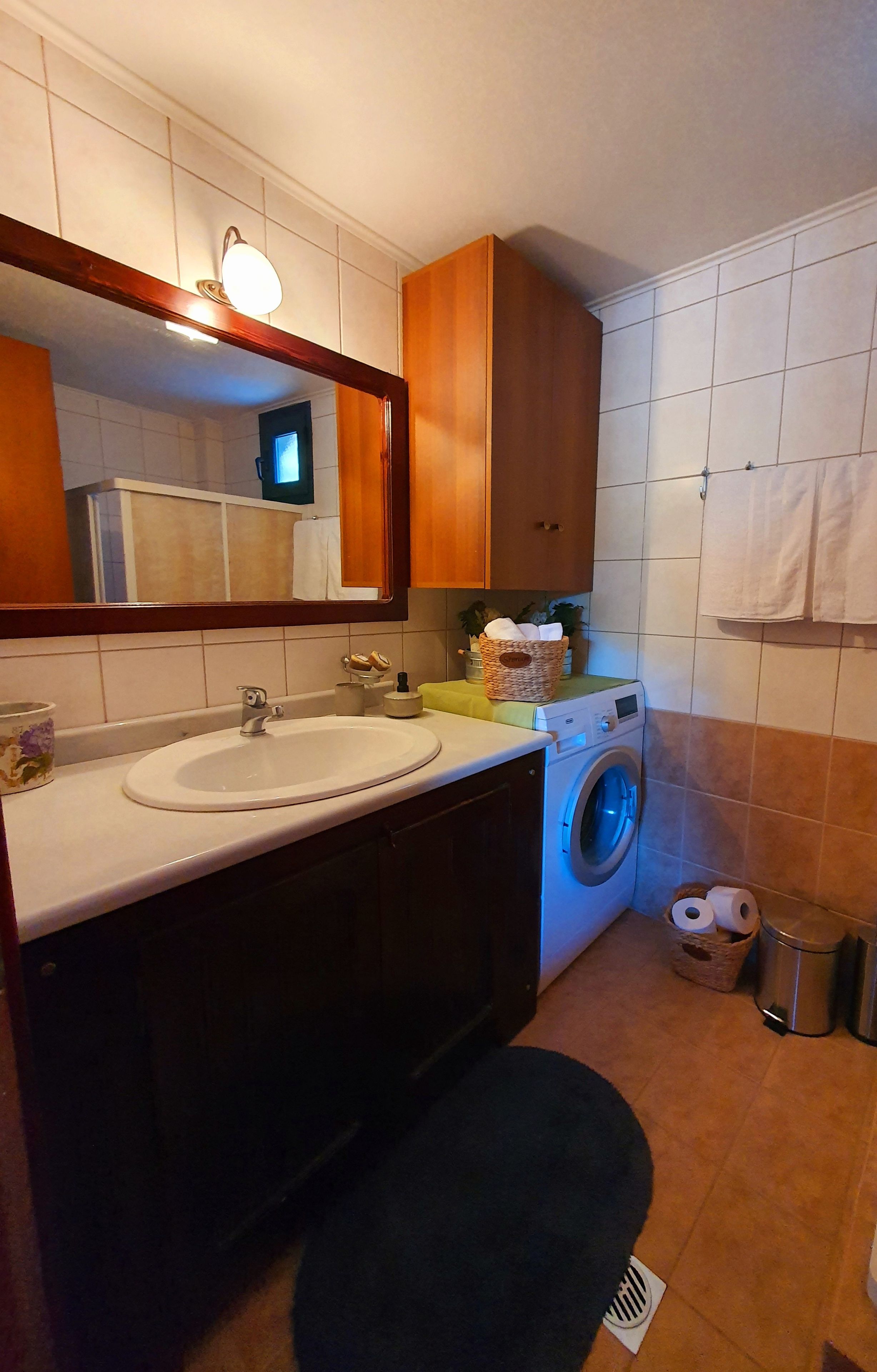 Ein kleines Badezimmer mit Waschbecken, Spiegel, Holzsärchen, einer Waschmaschine und einem Handtuchhalter.