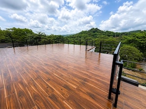 A spacious wooden deck with a metal railing, overlooking a lush green landscape. - Villa Bonita Lodge - San Juan Sur, NIC (El Sucio (San Juan del Sur))