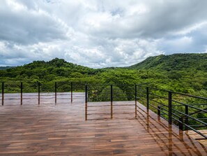 Une terrasse en bois avec une rambarde métallique, donnant sur une colline verdoyante.