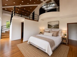 Une chambre avec un grand lit, une vue sur un tableau représentant un paysage, un escalier et un plancher en bois.
