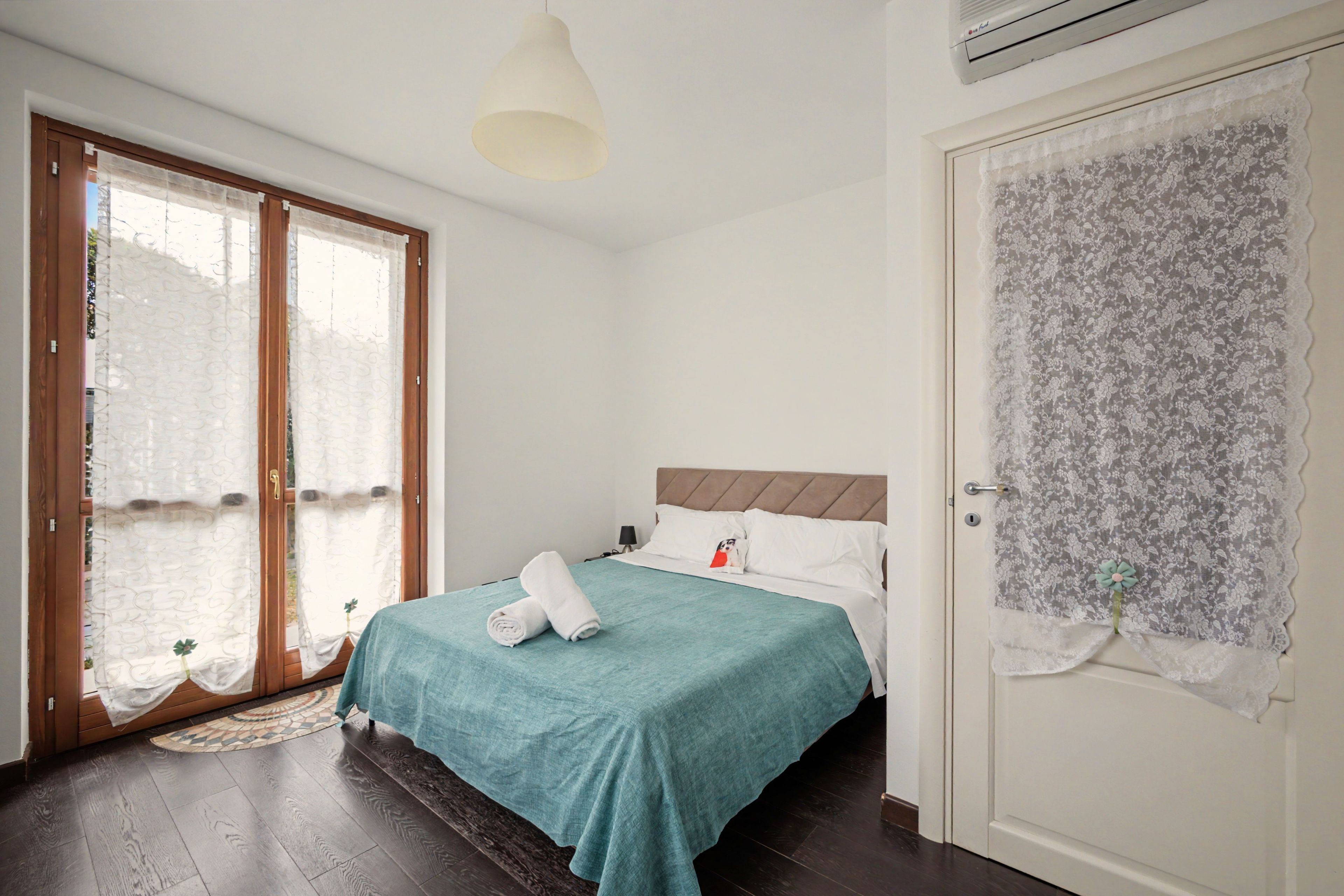 Ein Hotelzimmer mit einem Bett, einer Tür mit Spitzenvorhängen und einem Fenster mit gemusterten Vorhängen.