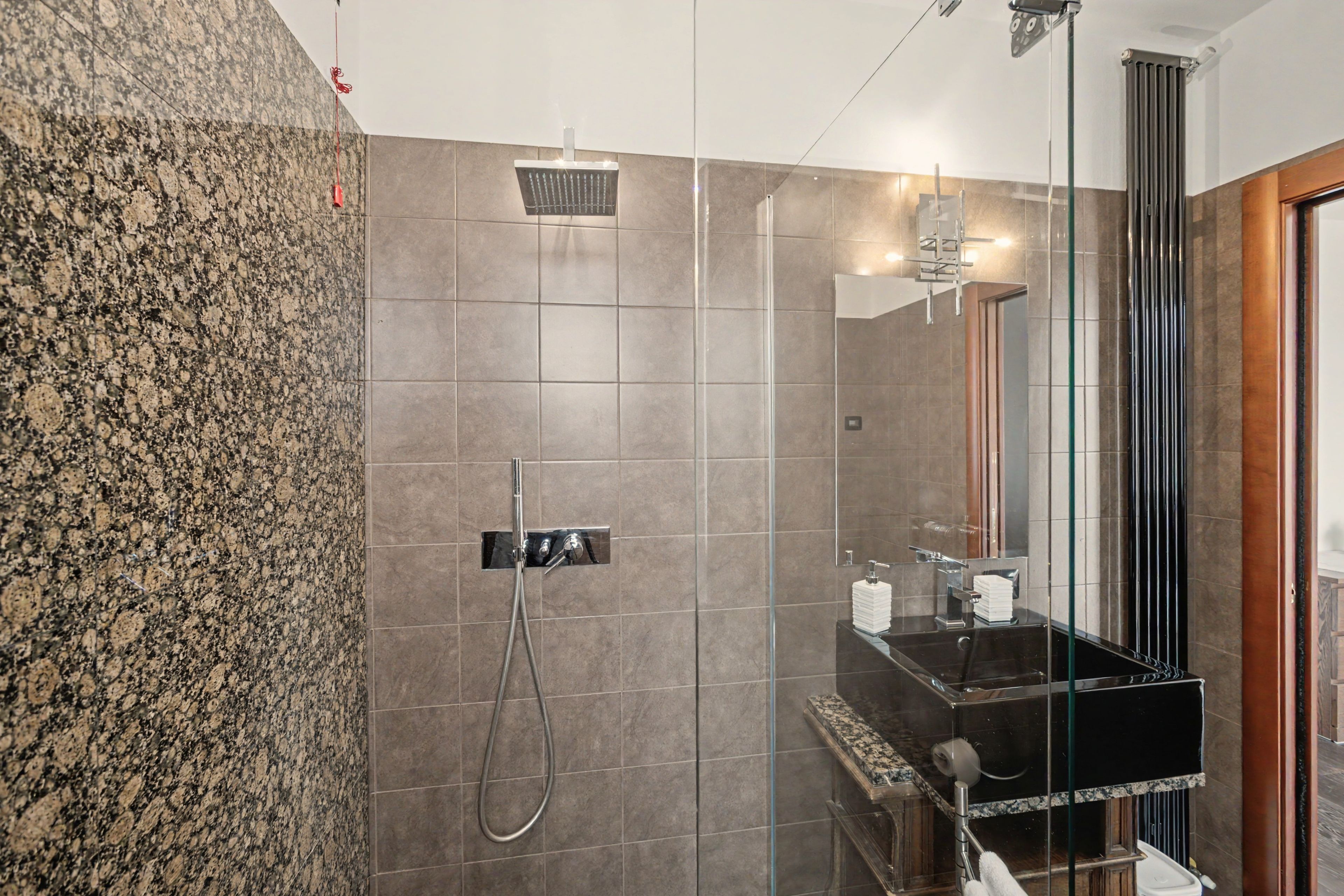 Un bagno moderno con doccia vetrata, lavabo nero su piano in marmo e uno specchio grande.