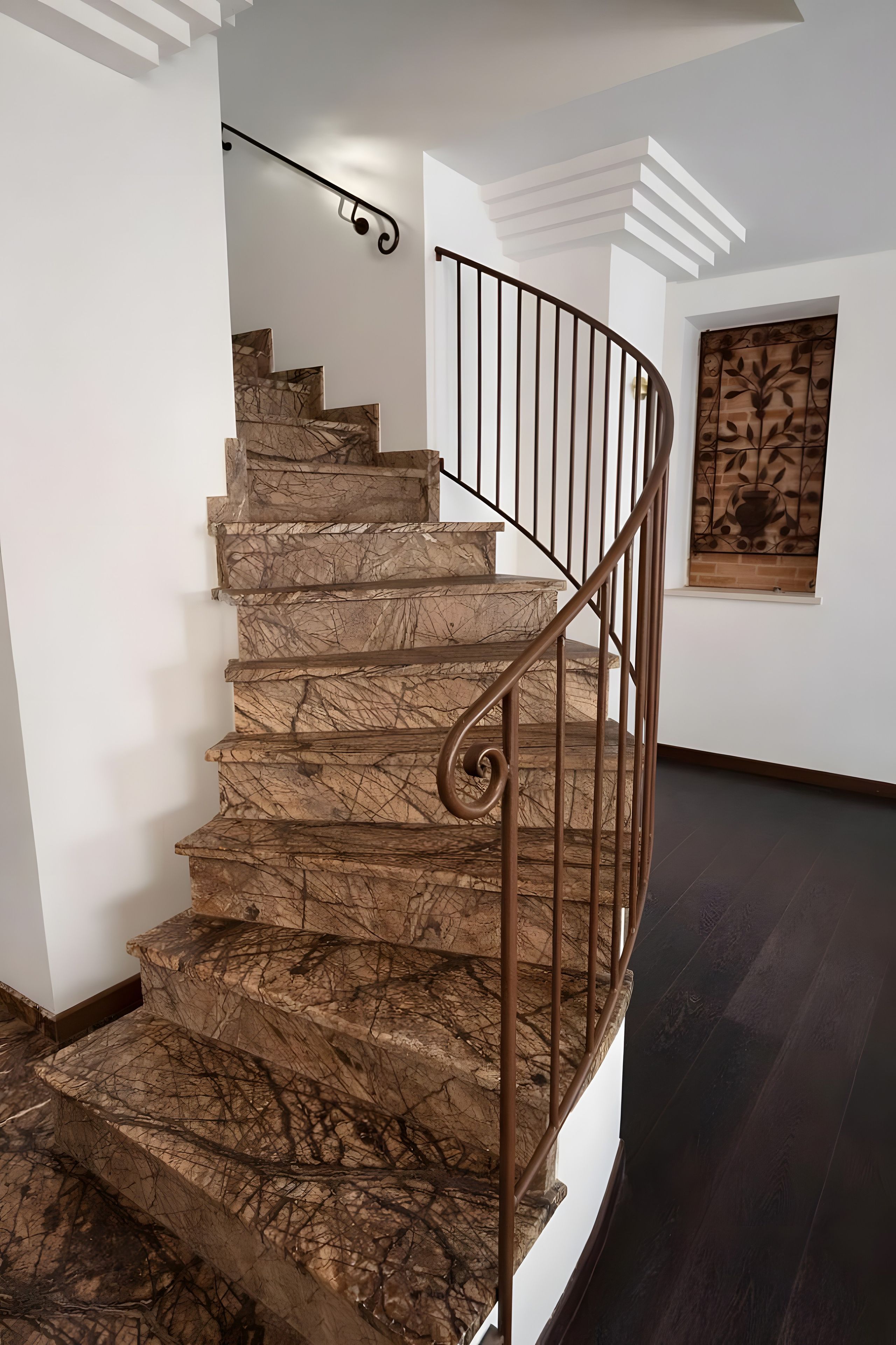 Escadaria em espiral com acabamento em mármore e corrimão de metal.