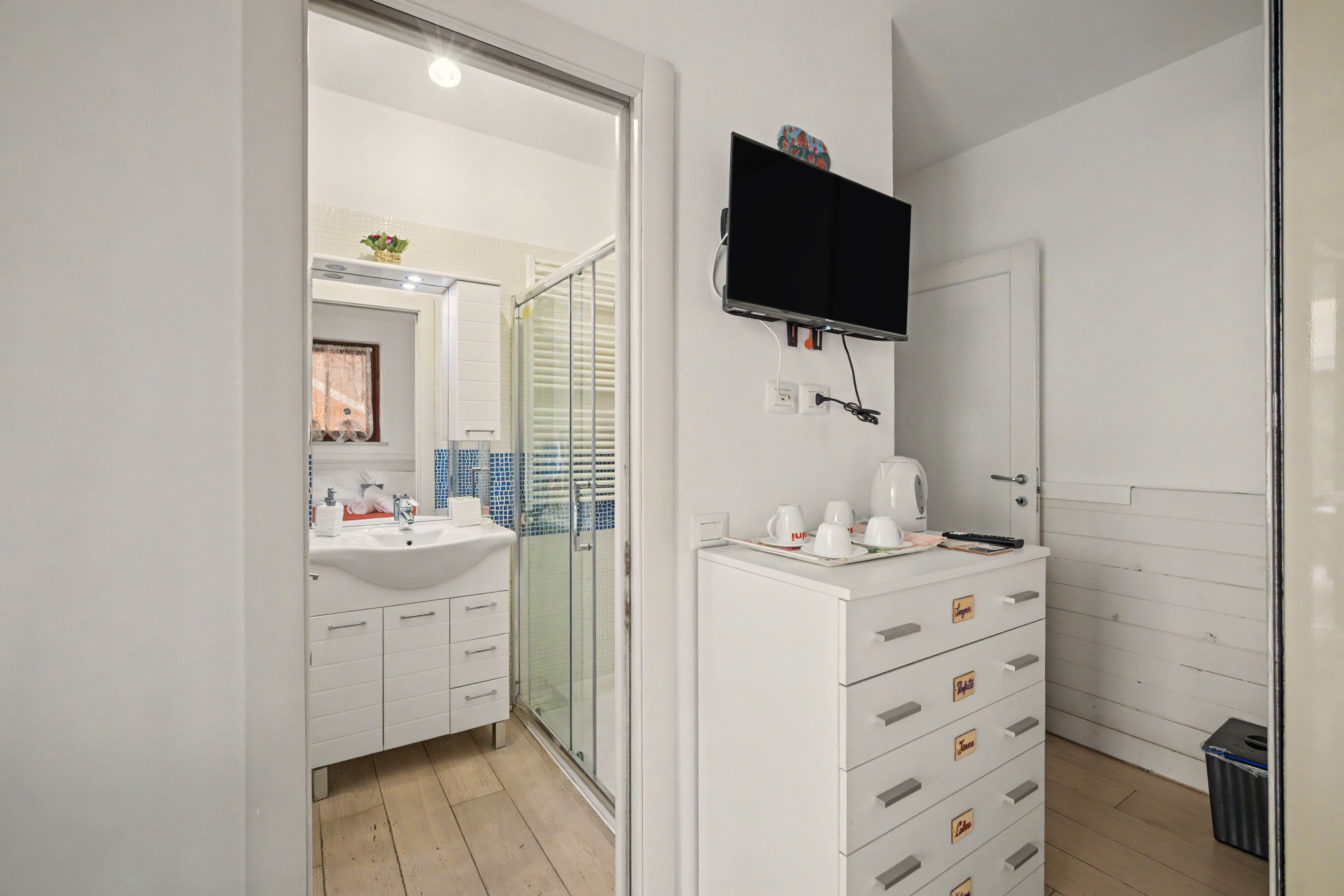 A modern bathroom with a white sink, mirror, and a flat-screen TV mounted above the vanity.