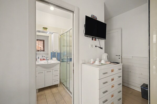 A modern bathroom with a white sink, mirror, and a flat-screen TV mounted above the vanity.