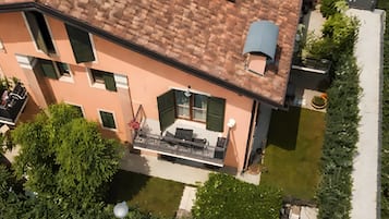 Un edificio de varios pisos con techo de tejas, un balcón con mobiliario exterior y un jardín bien cuidado.