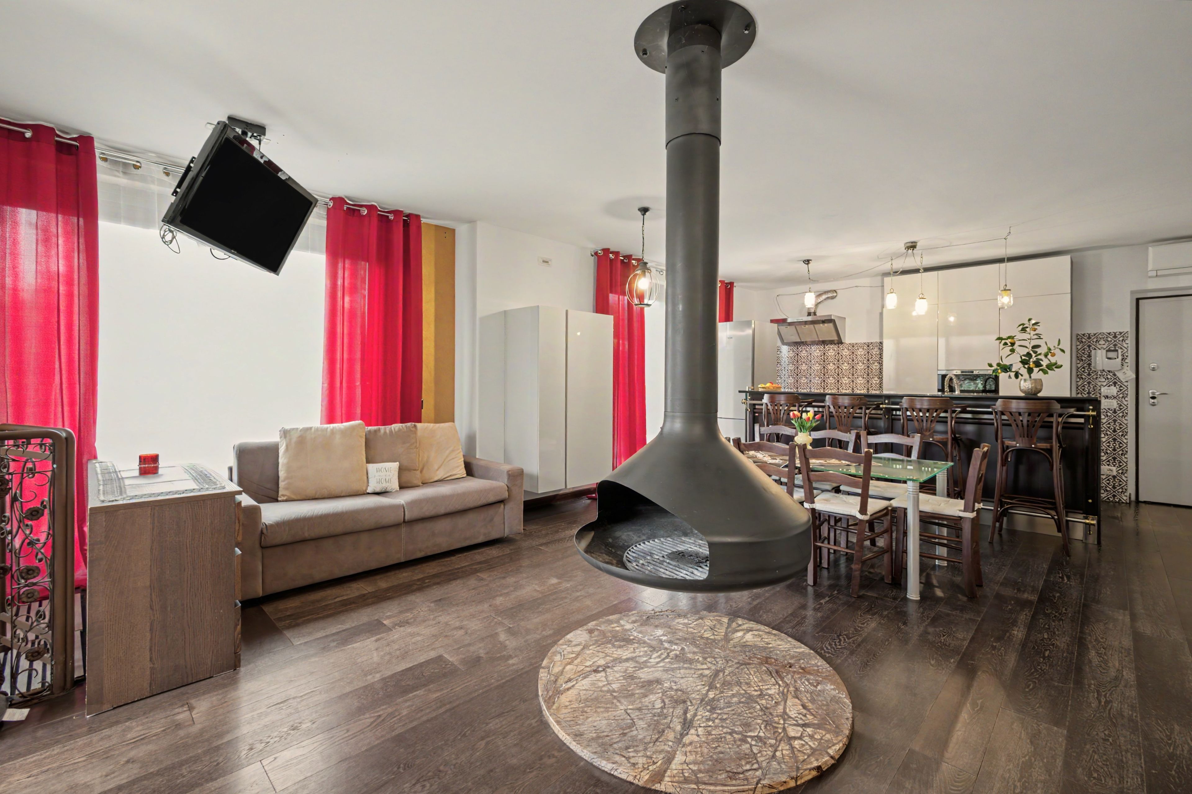 Ein modernes Wohnzimmer mit Kamin, einem Essbereich mit Glastisch und einer Küche im Hintergrund.