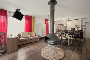 Ett modernt vardagsrum med en öppen spis, en matplats med ett glasbord och ett kök i bakgrunden.