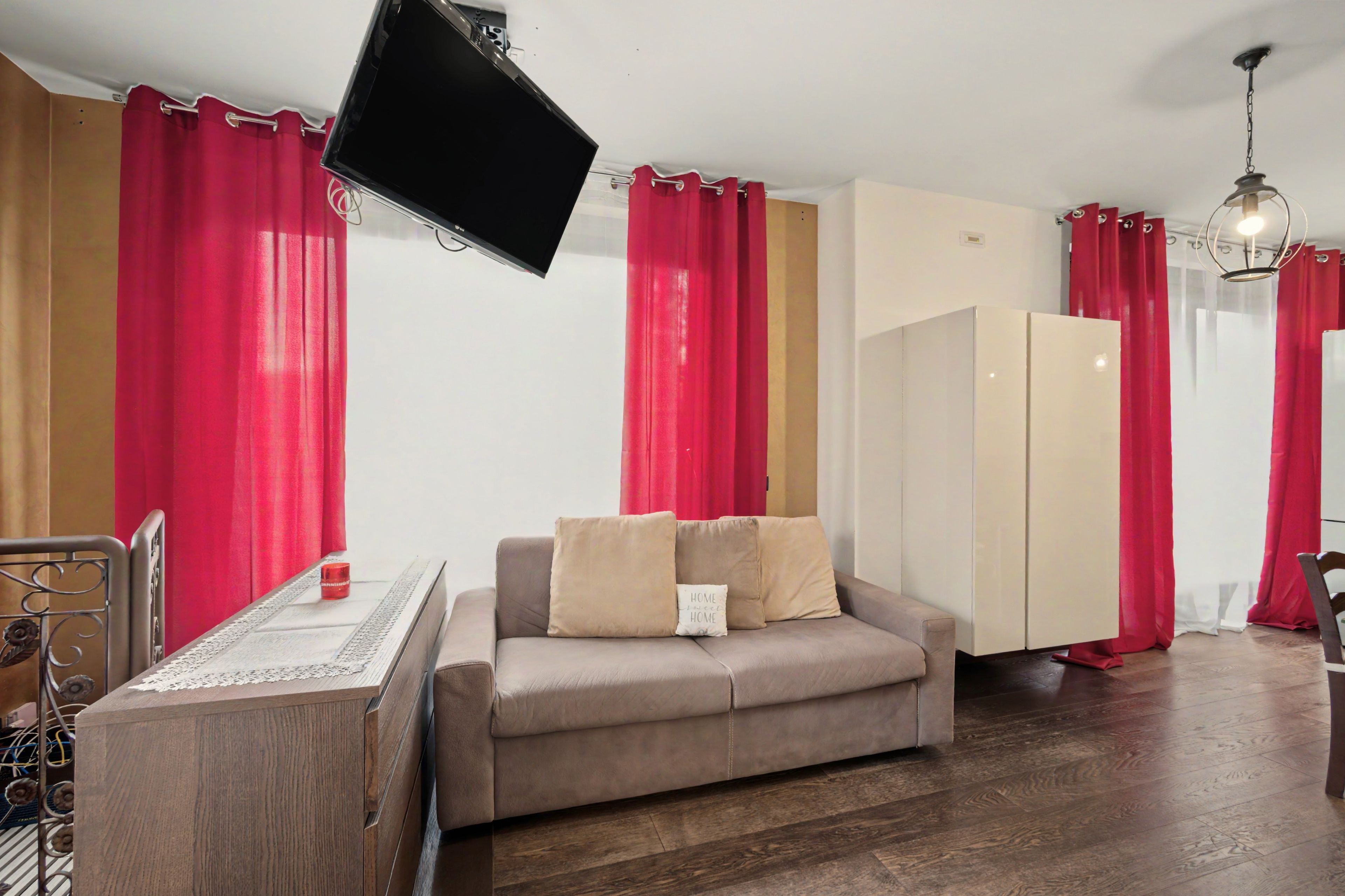 A room with a sofa, a television, a wardrobe, and a dining area with a table and chairs.