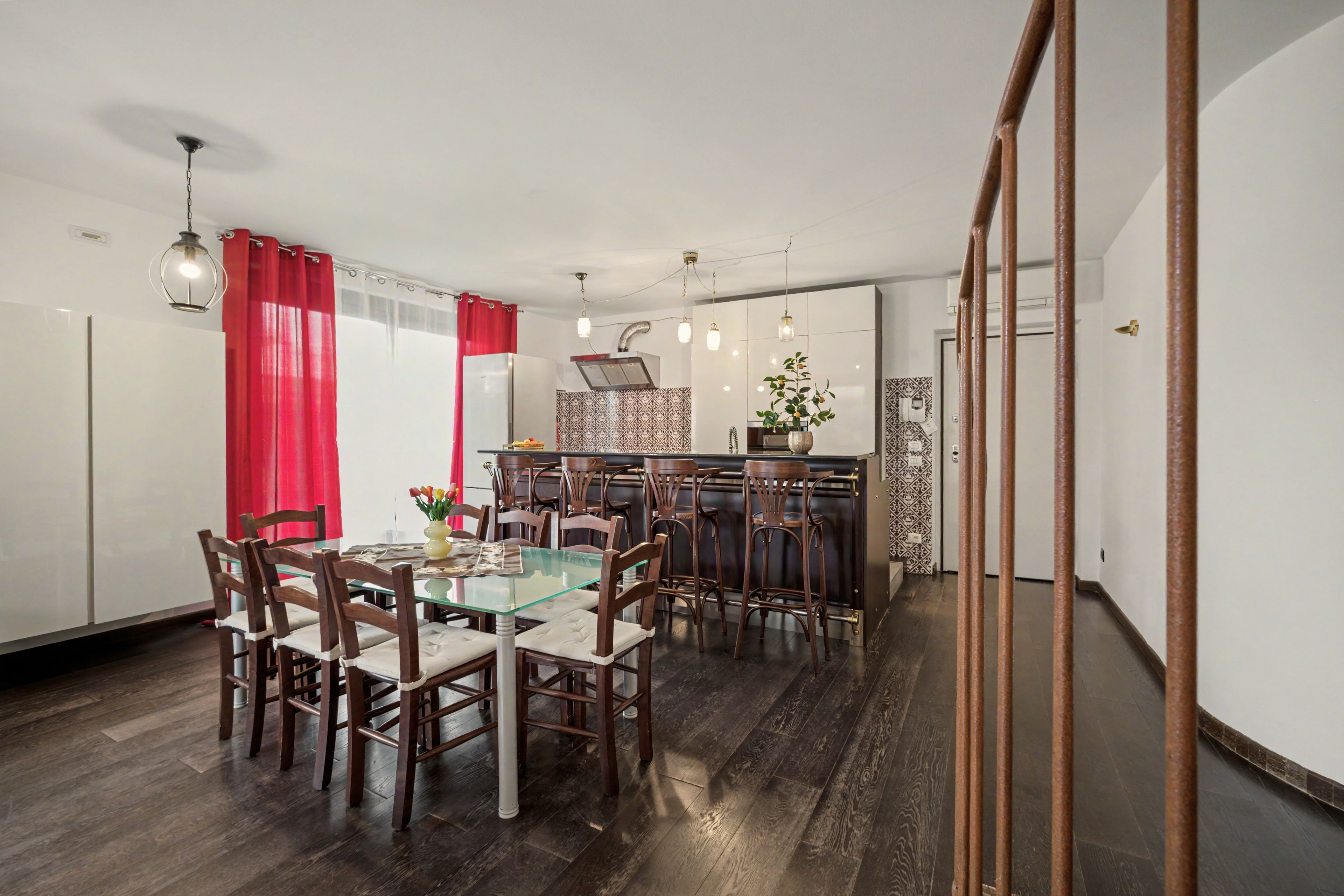 A dining area with a glass table, wooden chairs, and a kitchen in the background.