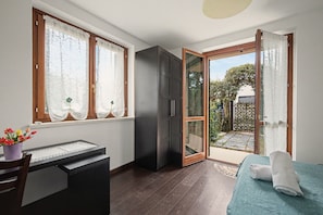A room with a bed, a desk, a wardrobe, and a sliding glass door leading to an outdoor area.