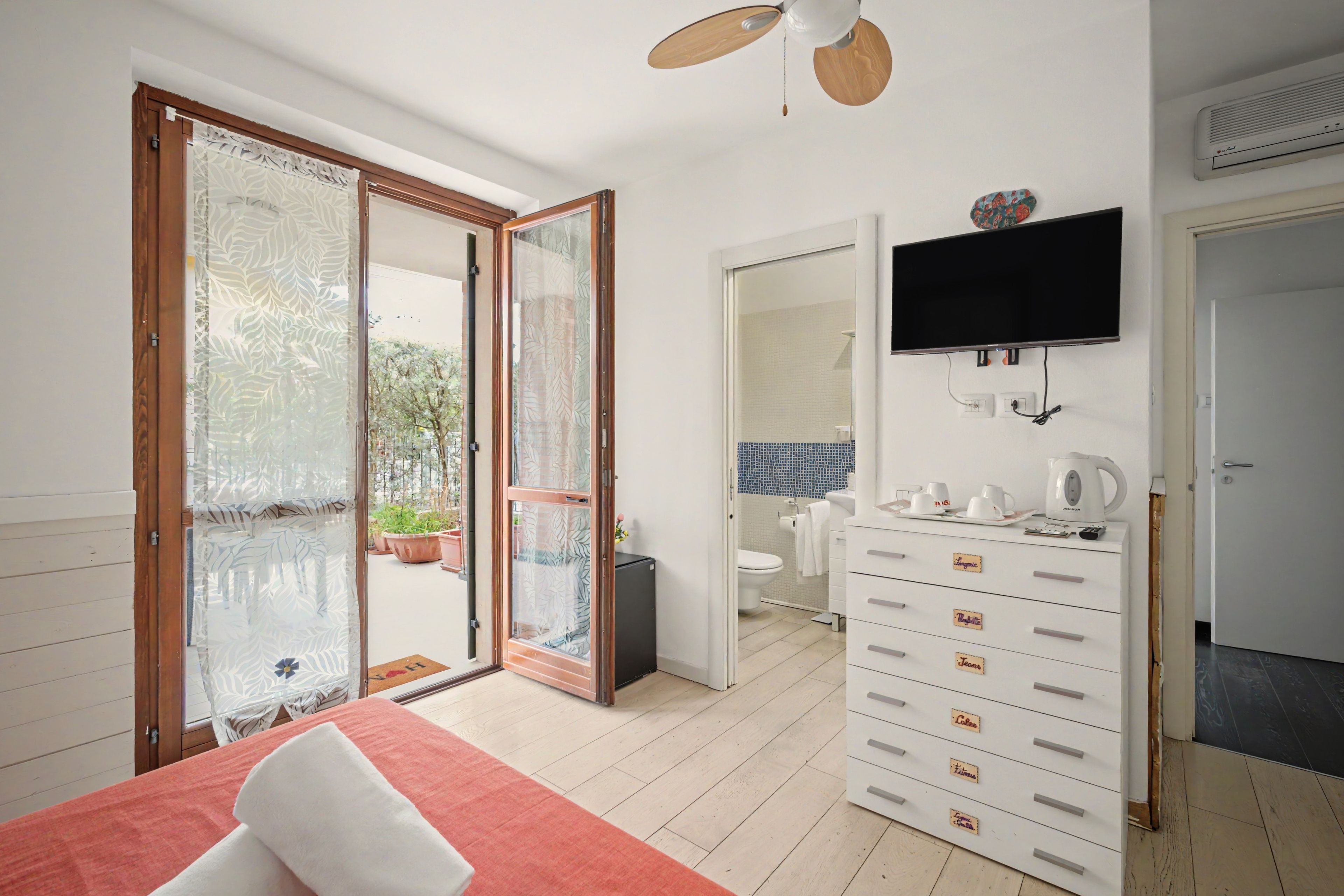 Ein Schlafzimmer mit einem Bett, einer Kommode, einem Fernseher und einer Glastür, die auf einen Balkon führt.