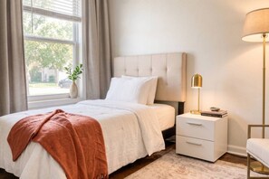 A bedroom with a bed, bedside table, lamp, and a window with curtains. - Two living rooms, cowboy pool and fire pit (Austin)