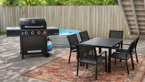 En udendørs terrasse med grill, et bord og stole.