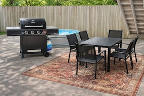 Un patio exterior con una parrilla, una mesa y sillas.