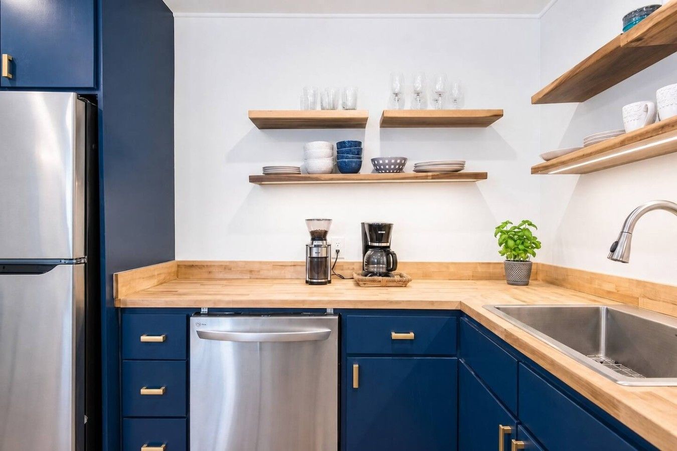 A modern kitchen with a stainless steel refrigerator, a coffee maker, and wooden shelves above the counter.