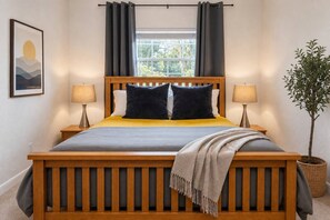 Una cama con estructura de madera, dos almohadas, un edredón y una lámpara de noche.