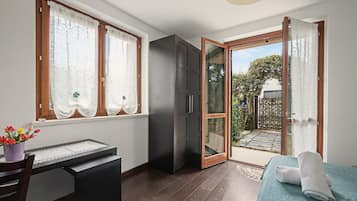 Een kamer met een bed, een bureau, een kledingkast en een glazen schuifdeur naar een tuin.