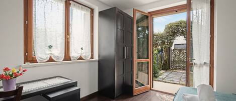 Una habitación con cama, escritorio, armario y puerta de cristal corredera que da a un jardín.